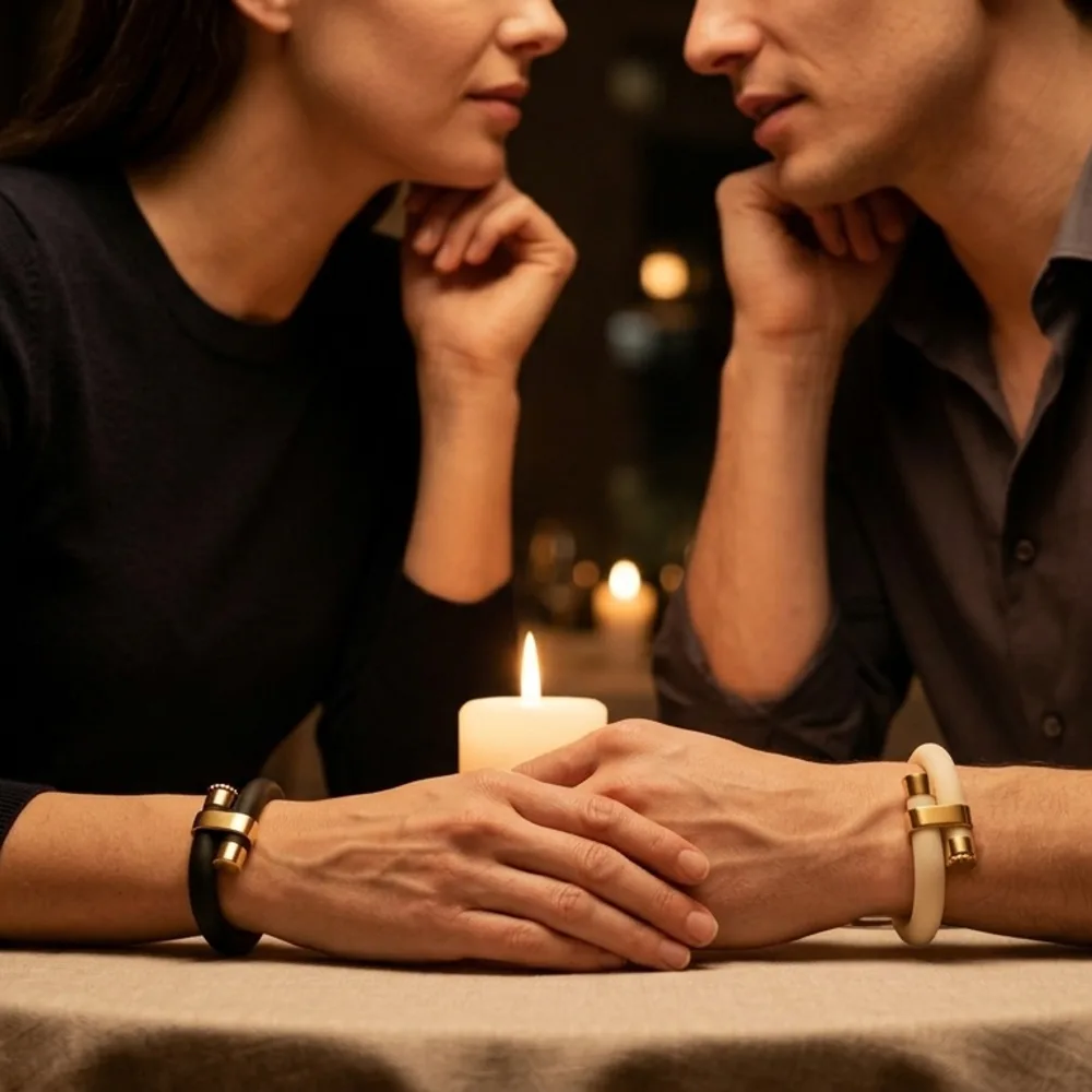 Close-up of a couple holding hands at a candlelit dinner, each wearing a wristraw in gold finish